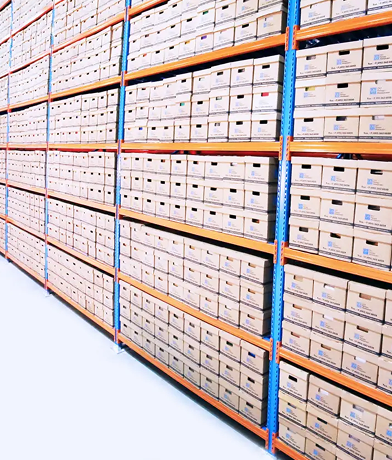 Duże regały magazynowe wypełnione rzędami oznakowanych kartonów w jasno oświetlonym magazynie. Pudełka są uporządkowane i ustawione na metalowych stojakach, co ułatwia przegląd regałów i efektywne przechowywanie.